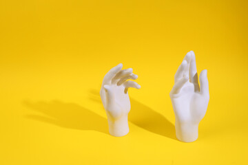 White plastic hands on a yellow background. Minimal layout