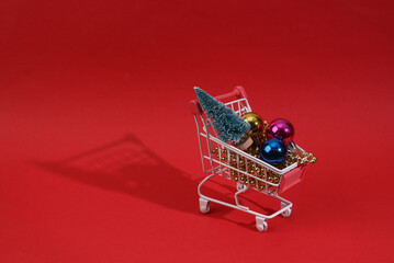 Mini shopping cart with christmas toys, Christmas tree and garlands on red background