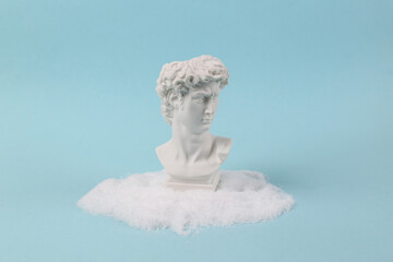 Plaster bust of David in a snowdrift on turquoise background. Minimal layout
