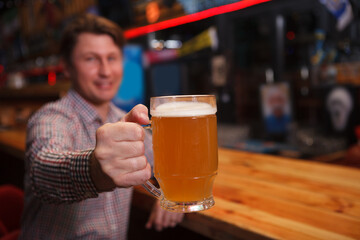 Happy man holding out beer glass to the camera, copy space