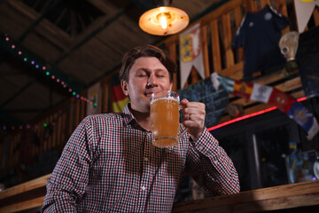Happy mature man enjoying aroma of craft beer in his glass, resting at beer pub