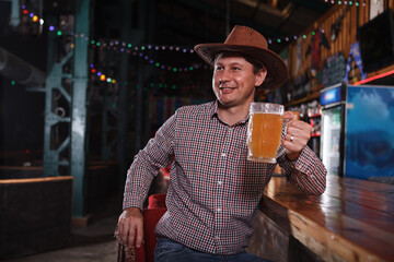 Happy mature cowboy toasting with beer glass, drinking at the bar