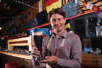 Cheerful mature male brewer smiling to the camera, holding beer glass
