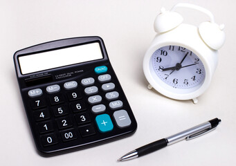 On a light desktop, there is a black calculator, a pen and a white alarm clock. Business concept