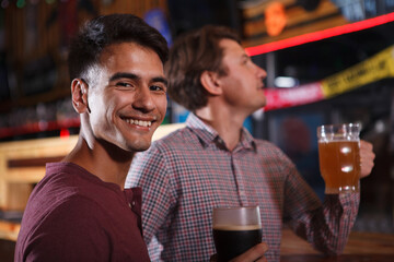 Handsome young man smiling to the camera while drinking beer with a friend