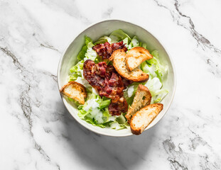 Alternative caesar salad with bacon on a light marble background, top view. Delicious brunch, snack