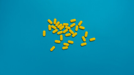 Yellow vitamins medicine capsules pills isolated on blue background.