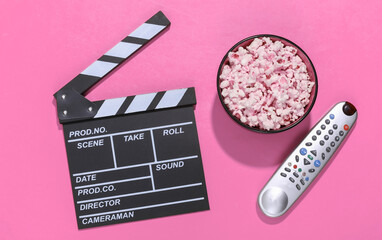 Movie clapper board, popcorn bowl, tv remote on pink background with deep shadows. Entertainment...