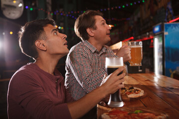 Two male friends having beer while watching match at beer pub