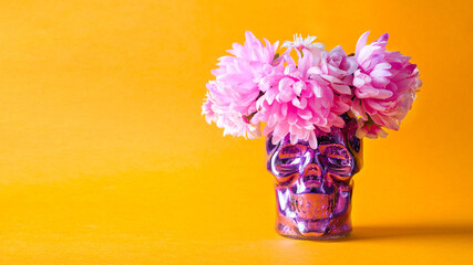 Decorations for the holiday Dia de Muertos. Decorative skull with a wreath of pink flowers on an orange background.