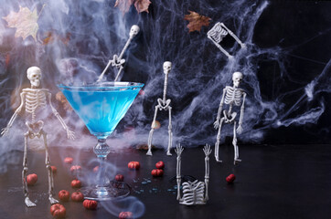 Halloween drink on a black background with skeletons, cobwebs, mini pumpkins and smoke. Selective...