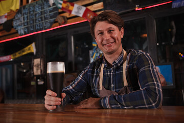 Happy mature male bartender smiling to the camera, working at his beer pub