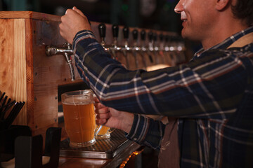 Cropped shot of a bartender pouring beer into glass from beer tap