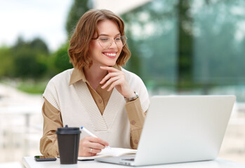 Beautiful young woman entrepreneur having cup of coffee while holding meeting online outside in cafe