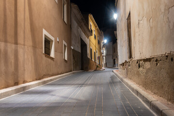 Obraz premium Narrow town street, empty and lit by streetlights at night.