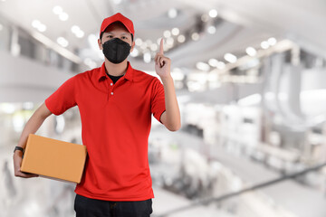Delivery Concept with face mask in red cloth holding a box package side view of postman or...
