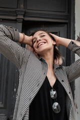 Funny young beautiful teenager model girl with cute smiles and happy emotions in a fashionable plaid shirt and glasses enjoy life on the street