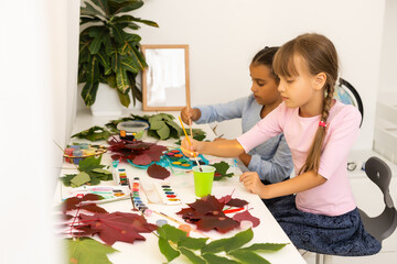 two schoolgirls draw leaves, girls paint autumn leaves