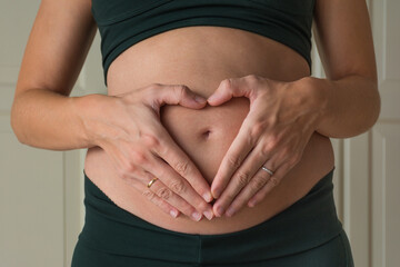 Pregnant woman forming a heart with her hands over her nude belly. 21 weeks. Isolated close-up over white background