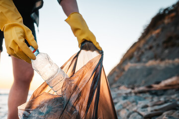 A woman volunteer puts a plastic bottle in a polyethylene bag. Close up of hands. In the background...