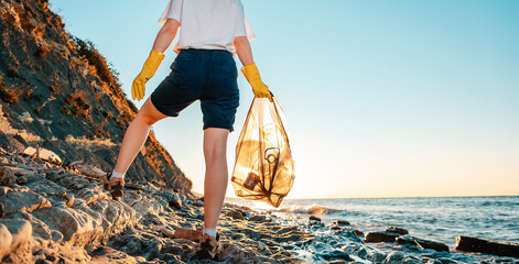 Close up of female volunteer holding a bag with garbage and plastic bottle in her hands. Back view....