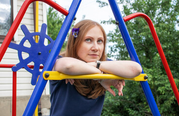portrait of a young girl with red hair and a flower in her hair, sitting on a children's playground
