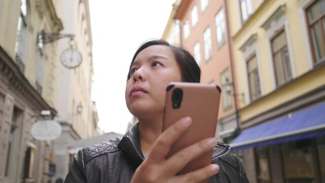 Asian woman standing and using smartphone to see map in town, getting lost in small town, Going out for a walk on the street in Sweden. Traveling abroad on long holiday