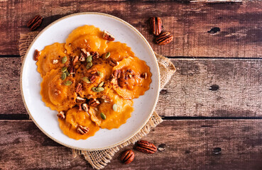 Pumpkin filled ravioli pasta with nuts and pumpkin seeds. Table scene, top view on a dark wood...