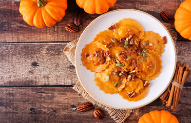 Pumpkin filled ravioli pasta with nuts and pumpkin seeds. Top view on a rustic wood background....