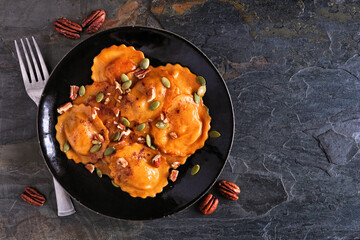 Pumpkin filled ravioli pasta with nuts and pumpkin seeds. Overhead view on a dark slate background....