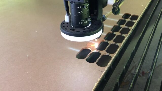Laser cutting machine for acrylic sheet metal. close-up. modern machine with CNC Co2 laser is cutting patterns on acrylic sheet  plate. bright burning sparks fly from laser beam during cutting process