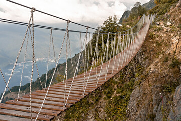 Suspended wooden bridge hanging over an abyss in mountain canyon and clouds, Extreme hike at...