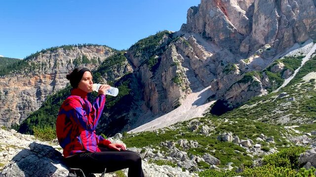 Female hiker tourist traveler woman drinking on a mountain path with the dolomites in the background,  Fanes Sennes Prags National Park, South Tyrol, Italy