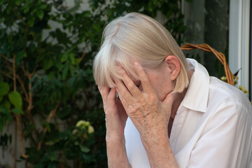 Close-up of a senior woman with white hair with her face buried in her hands because of a headache / depression / exhaustion
