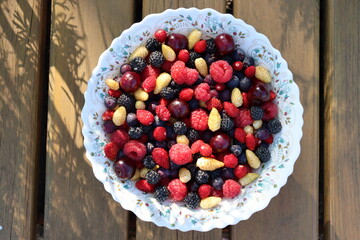 Berry mix in a white plate with a pattern. Cherries, white and red strawberries, black and red raspberries, shadberry. Summer kitchen, new harvest. Selective focus.