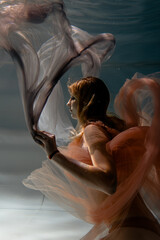 A girl with long dark hair swims underwater in a pink dress and with a crown on her head, like an underwater queen. Fairy tale suitable for advertising	
