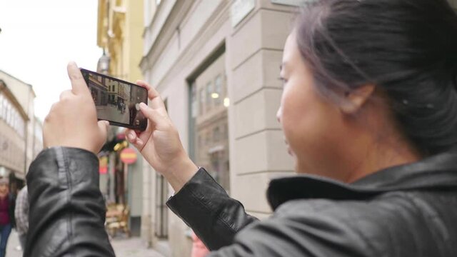 Asian woman standing and taking a picture of town in Sweden, traveling abroad on holiday. Using smartphone to take a photo. Beautiful town in Sweden