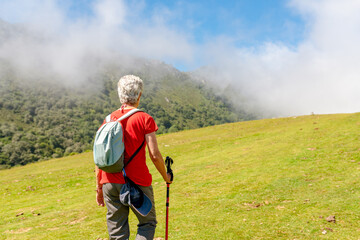 Elderly hiker walks across a hillside on a foggy sunny day.