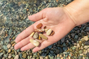 Close-up of a woman's hand holding a pebble on the beach. Sea, summer, vacation.