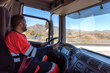 Truck driver in the driving position with both hands holding the steering wheel and driving.