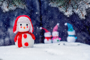 A lone snowman at a distance from other snowmen in the woods during a snowfall