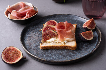 Crostini with Italian ham and ricotta, toast with prosciutto and figs on a dark background.