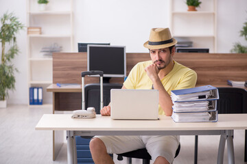 Young male employee preparing for trip at workplace