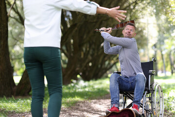 Fototapeta premium Disabled man in wheelchair is swinging violin at woman in park
