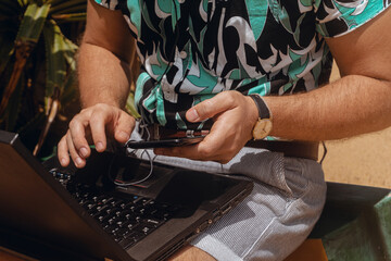 Cyfrowy nomada, mężczyzna pracujący na tropikalnej plaży z laptopem i telefonem. - obrazy, fototapety, plakaty