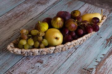 Still life with fruits pears and plums lie on a wicker plate in the form of a boat which stands on boards in the style of Provence against the wall