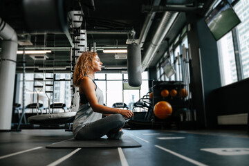 Fototapeta na wymiar Young attractive woman is doing yoga in a dark gym sitting on the floor in a lotus position meditating. Concept of a healthy lifestyle.