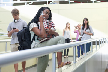 Fototapeta premium Female student on smartphone holding pile of books