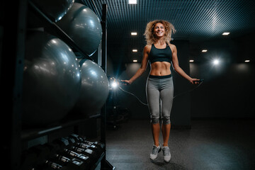 Slender athlete is engaged in cardio training in a black colored gym jumping on a rope. Concept of...