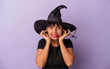 Young mixed race woman disguised as a witch isolated on purple background  covering ears with hands.